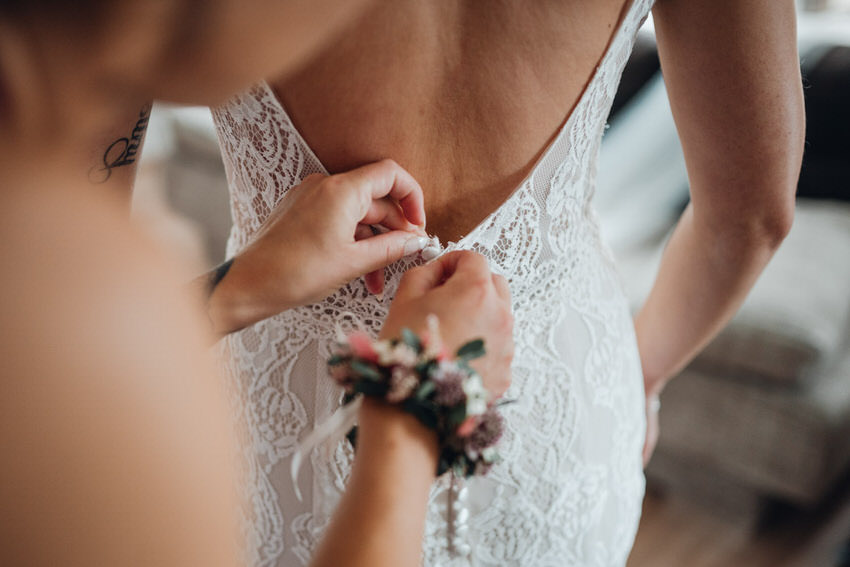 Braut wird das Hochzeitskleid zugeknöpft – gesehen bei frauimmer-herrewig.de